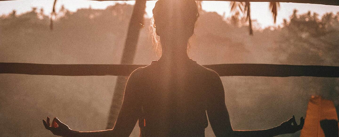 Mujer meditando frente a una puesta de sol